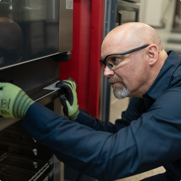 Technician in safety glasses and gloves inspecting a commercial oven door