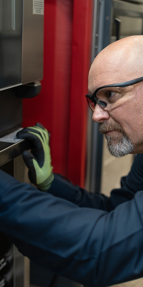 Technician in safety glasses and gloves inspecting a commercial oven door