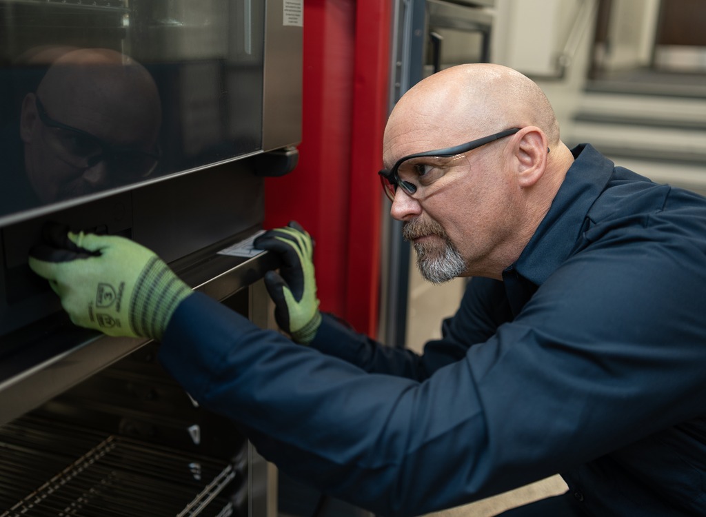 Technician in safety glasses and gloves inspecting a commercial oven door
