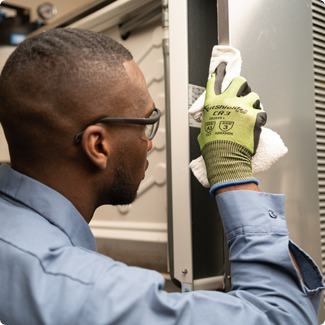 Technician in safety glasses examining a part while servicing commercial kitchen equipment
