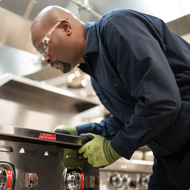Technician in safety glasses leaning over to service a commercial range