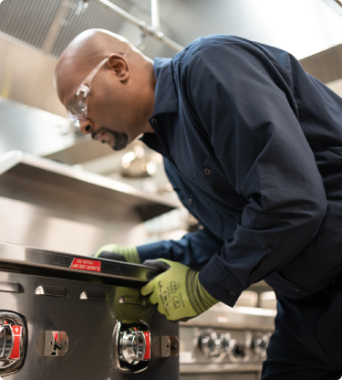 Technician in safety glasses leaning over to service a commercial range