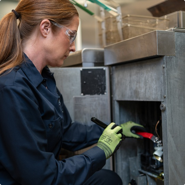 Technician using a tool on the lower access panel of commercial kitchen equipment