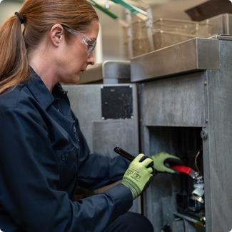 Technician using a tool on the lower access panel of commercial kitchen equipment