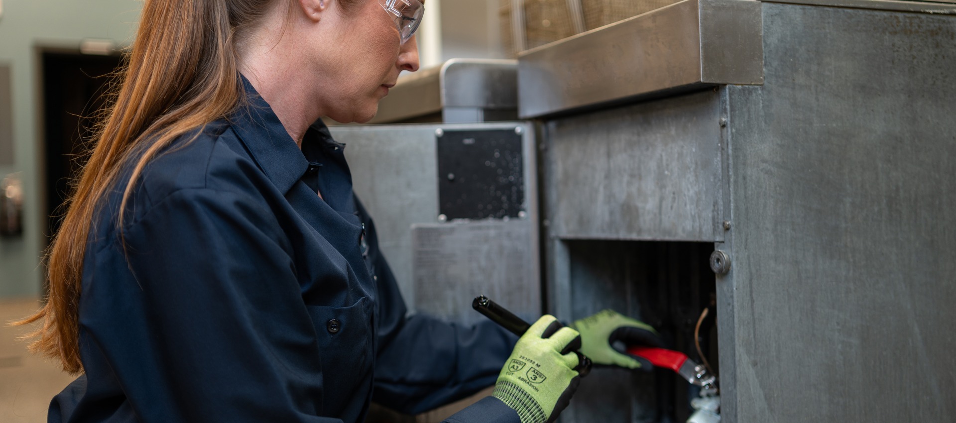 Technician using a tool on the lower access panel of commercial kitchen equipment