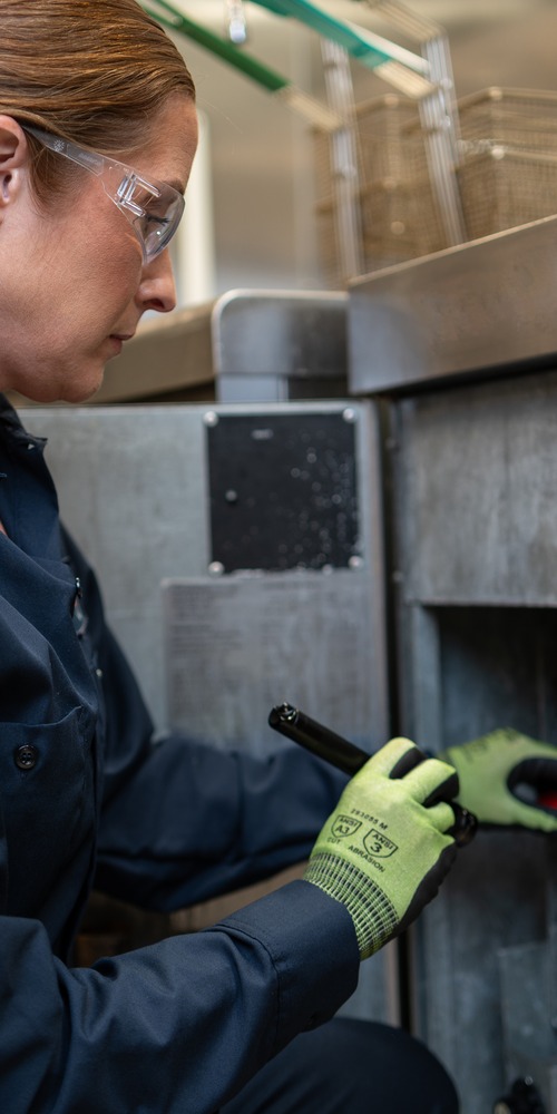 Technician using a tool on the lower access panel of commercial kitchen equipment