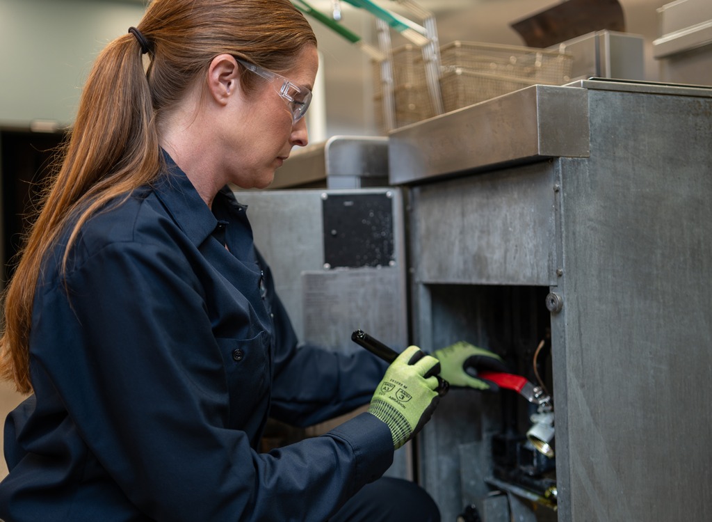 Technician using a tool on the lower access panel of commercial kitchen equipment