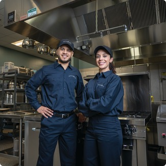 Two Total Tech technicians in uniform standing in a commercial kitchen