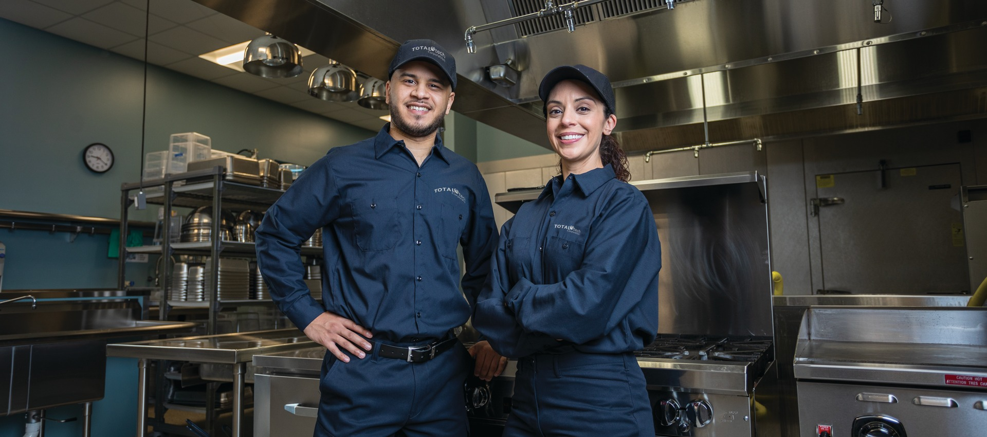 Two Total Tech technicians in uniform standing in a commercial kitchen