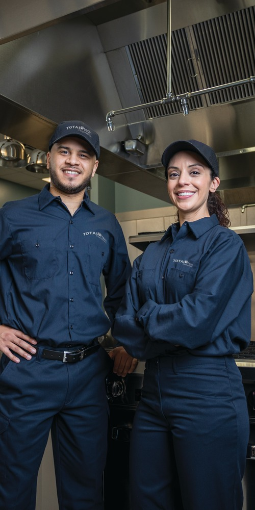 Two Total Tech technicians in uniform standing in a commercial kitchen