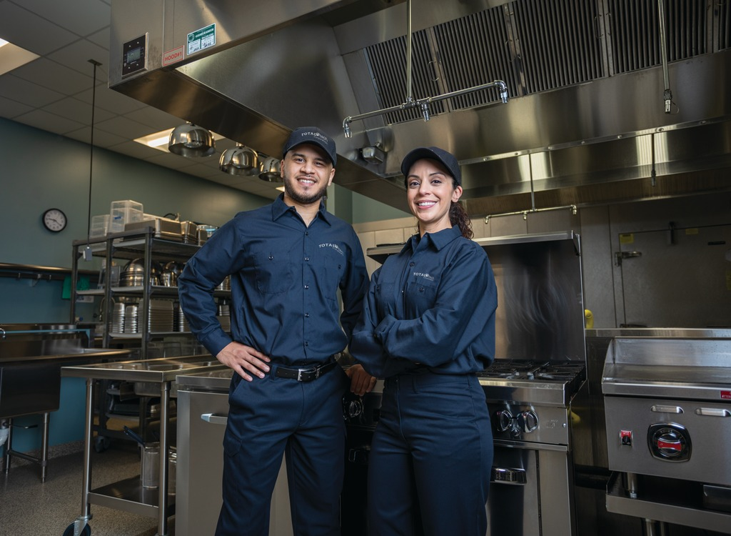 Two Total Tech technicians in uniform standing in a commercial kitchen