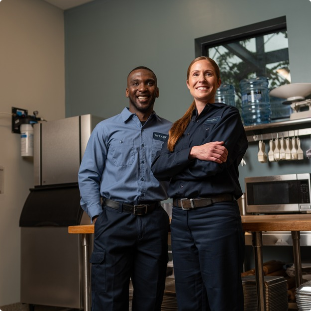 Two smiling Total Tech technicians standing side by side in a commercial kitchen