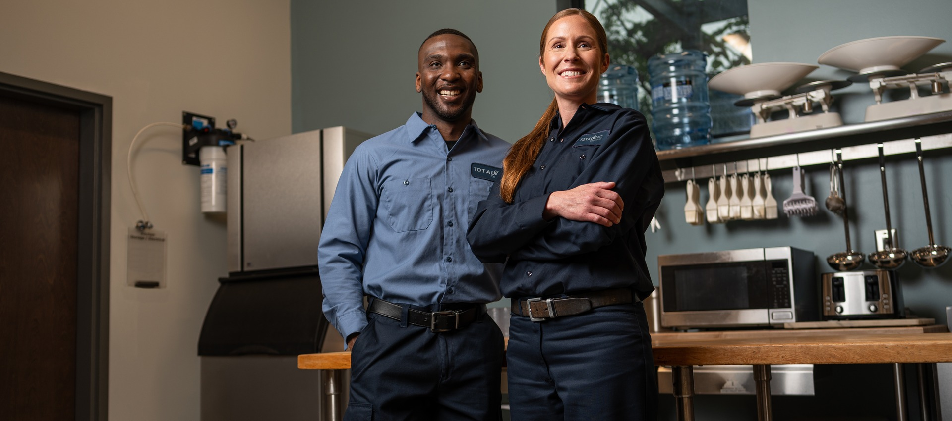 Two smiling Total Tech technicians standing side by side in a commercial kitchen