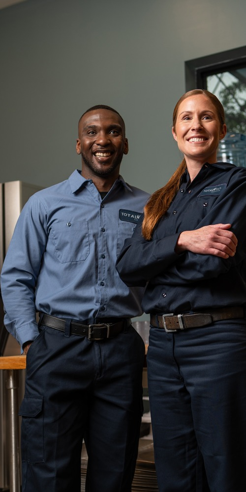 Two smiling Total Tech technicians standing side by side in a commercial kitchen