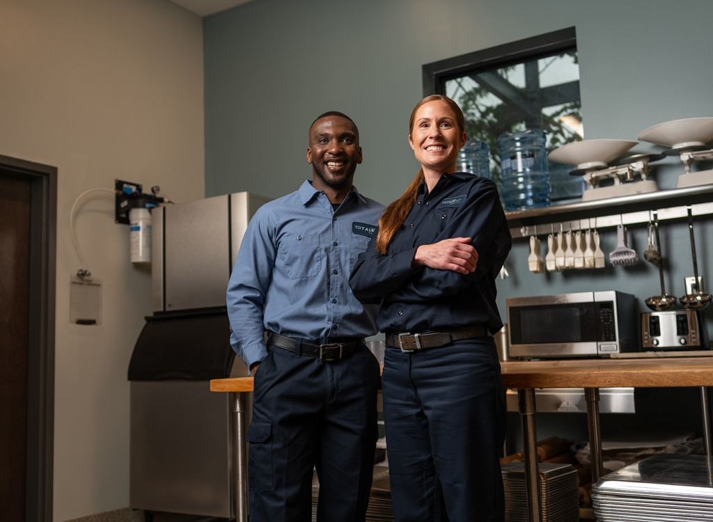 Two smiling Total Tech technicians standing side by side in a commercial kitchen
