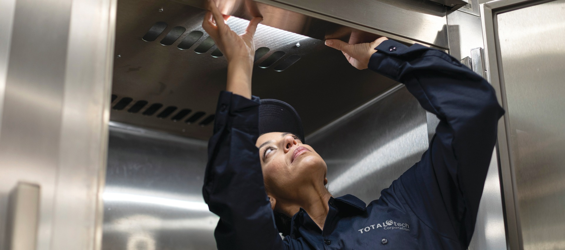 Total Tech technician reaching up to inspect a commercial kitchen exhaust hood