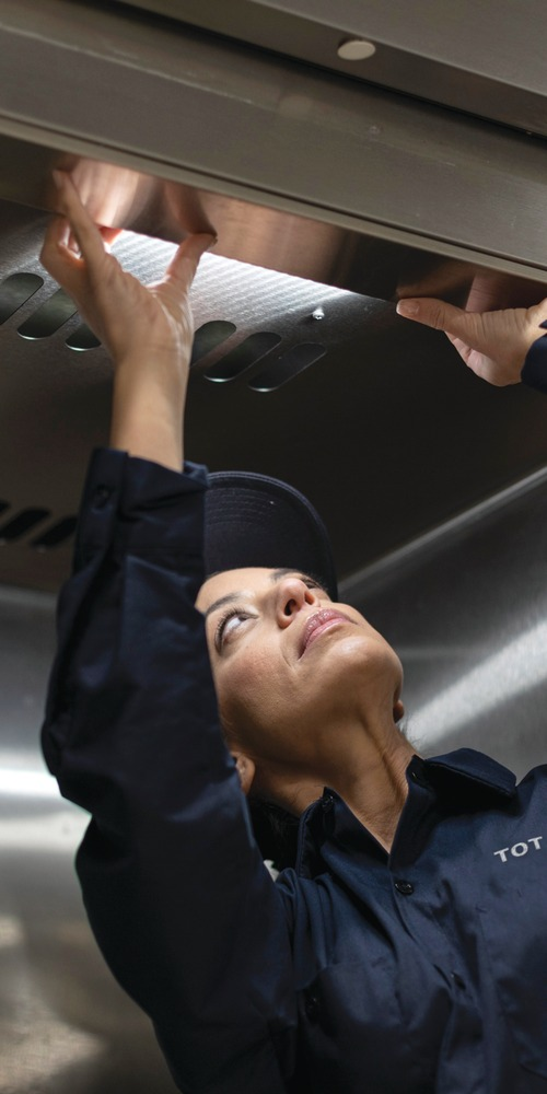 Total Tech technician reaching up to inspect a commercial kitchen exhaust hood