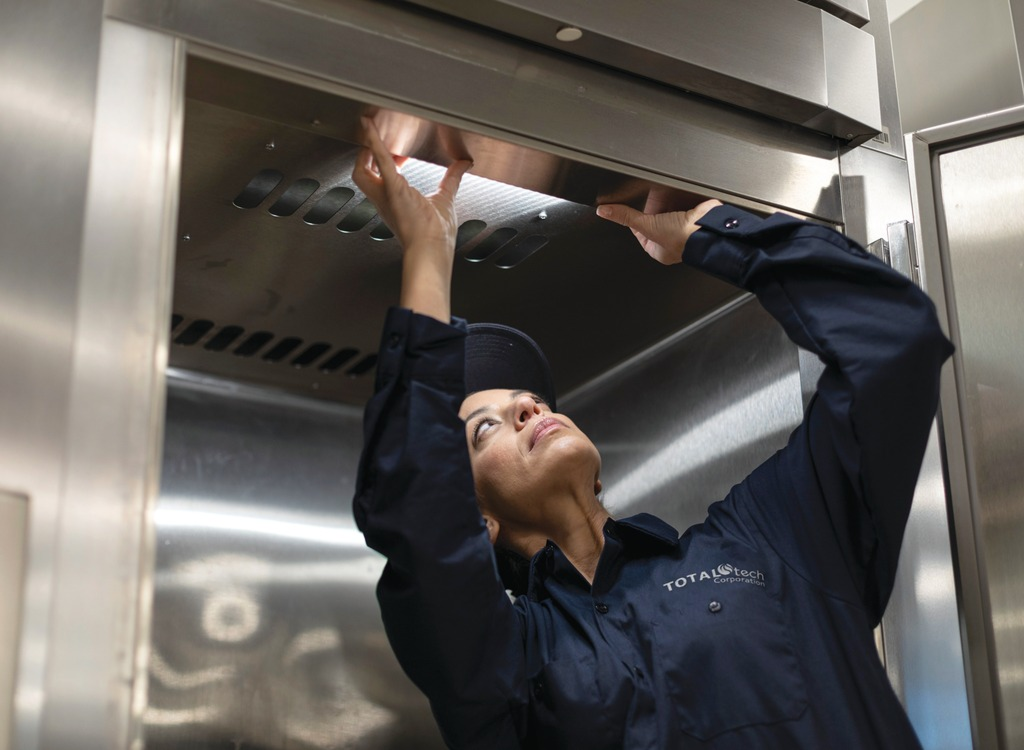 Total Tech technician reaching up to inspect a commercial kitchen exhaust hood