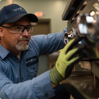 Total Tech technician in a cap and safety glasses working on commercial cooking equipment