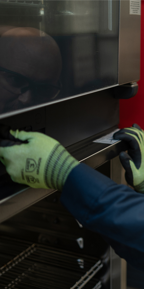 Technician in safety glasses and gloves inspecting a commercial oven door