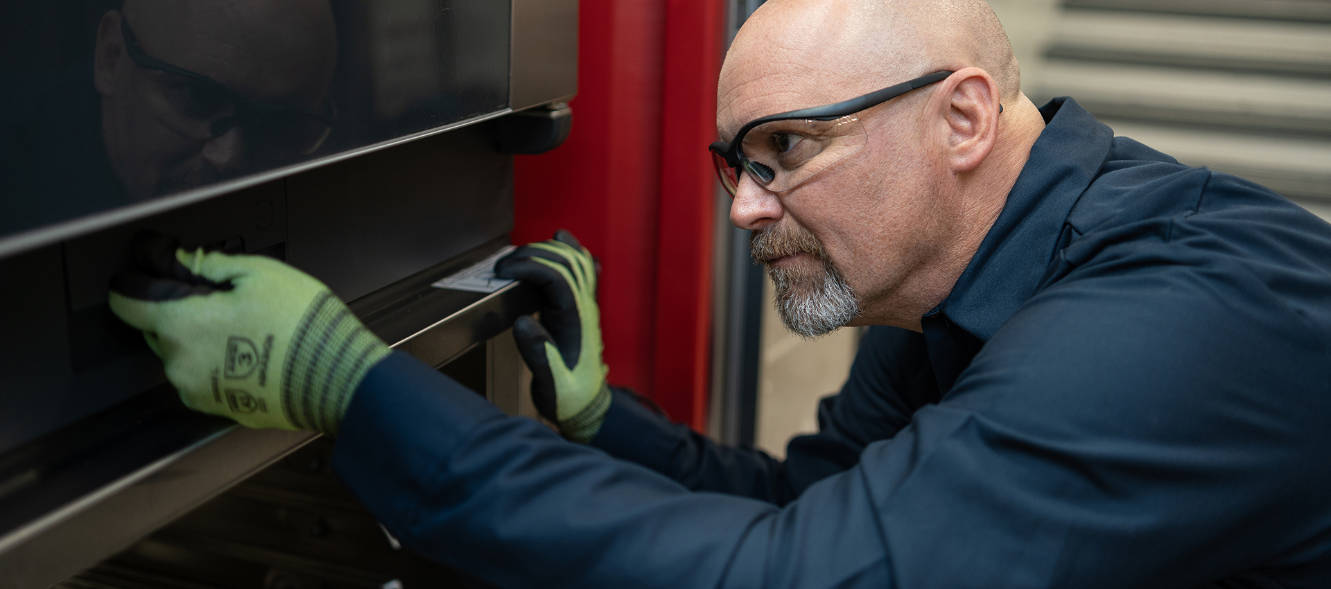 Technician in safety glasses and gloves inspecting a commercial oven door