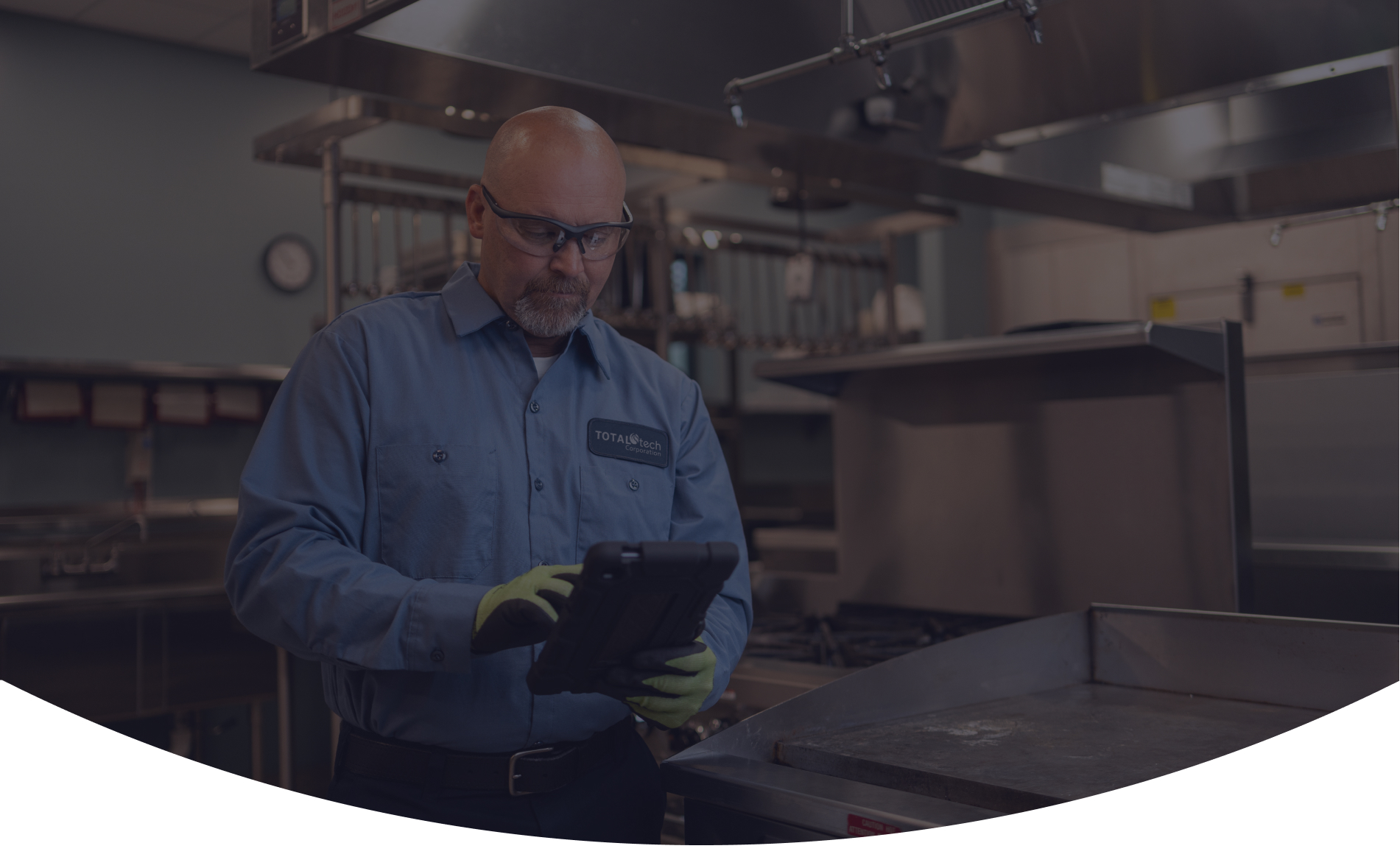 Total Tech technician in a work uniform checking a tablet in a commercial kitchen