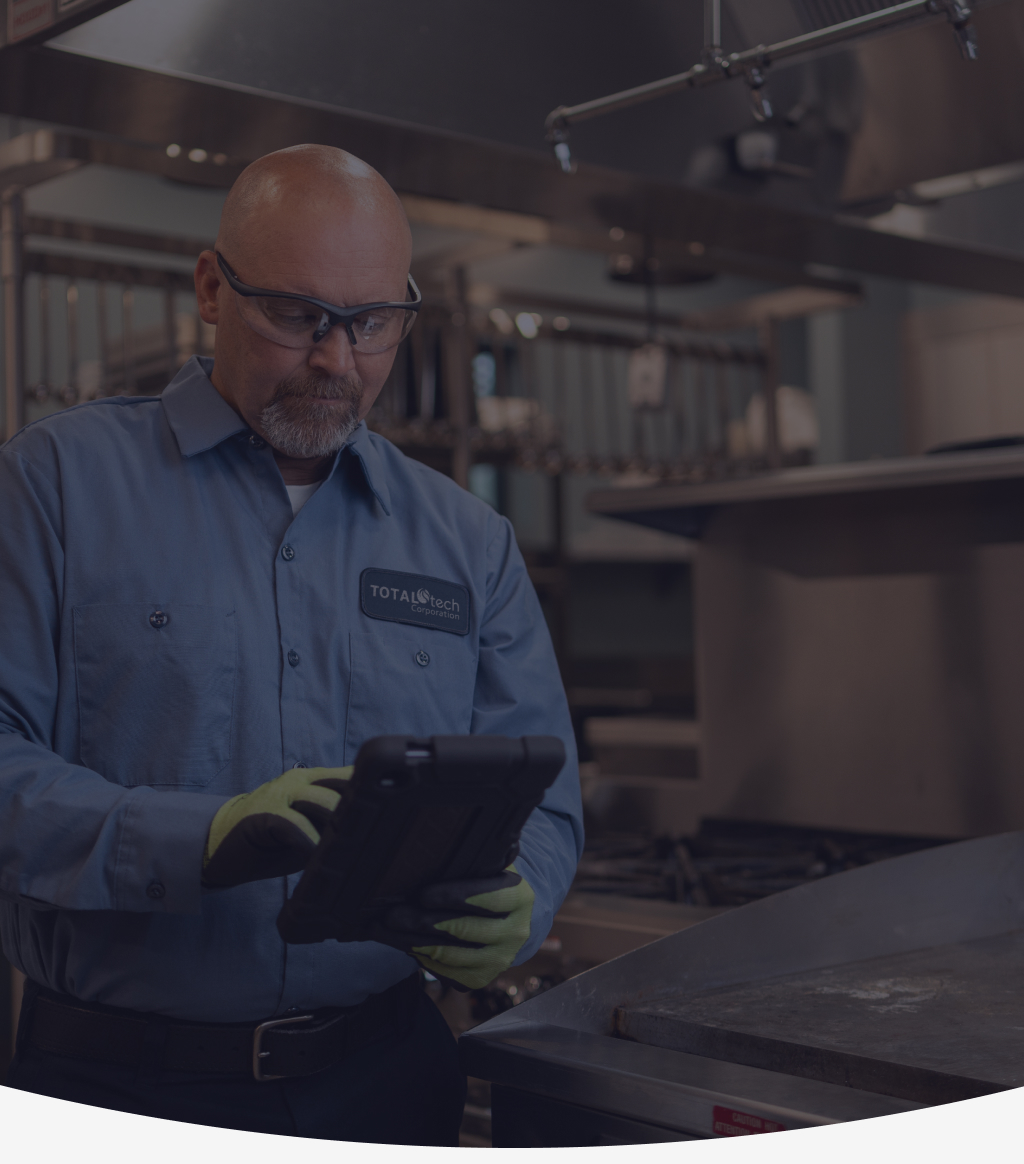 Total Tech technician in a work uniform checking a tablet in a commercial kitchen