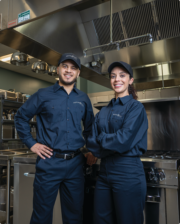 Two Total Tech technicians in uniform standing in a commercial kitchen